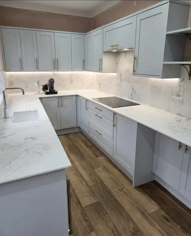 Duck-egg blue shaker kitchen with marble-effect worktops and splashback, brass handles, LED lighting and a wood-effect floor